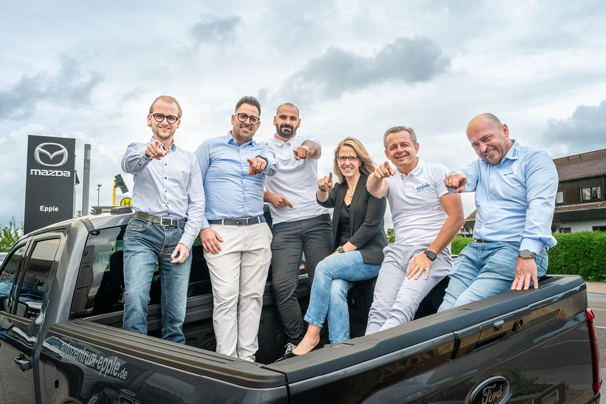 Mitarbeiter stehen auf der Ladefläche eines Ford und zeigen zur Kamera