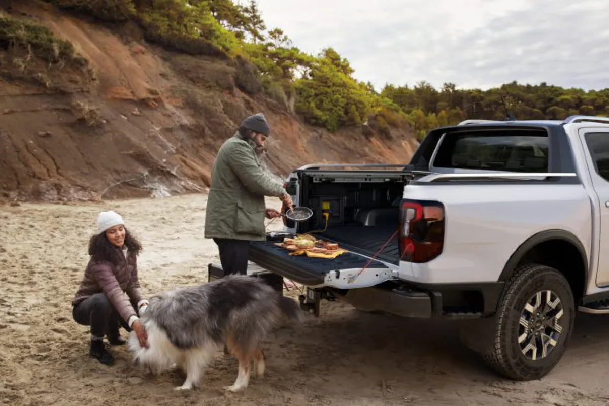 Mann macht Essen auf der Ladefläche eines Ford Rangers, daneben streichelt eine Frau einen Hund